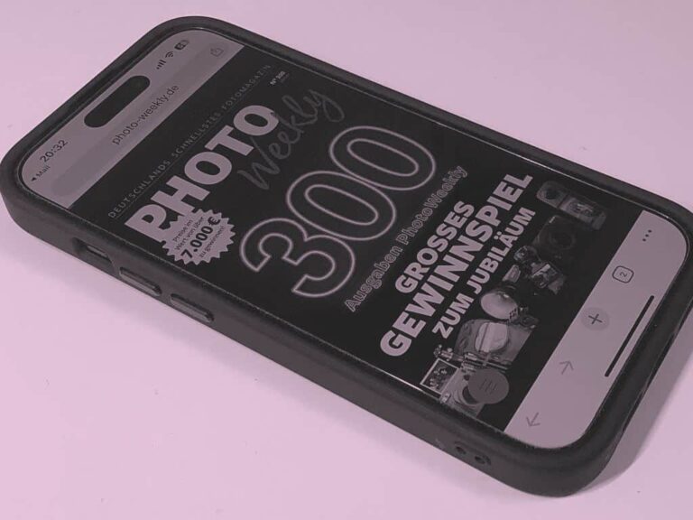 Ein Smartphone zeigt eine deutsche Zeitschrift mit dem Titel PHOTO Weekly 300 an, auf der Wettbewerbsdetails und Kameras abgebildet sind.