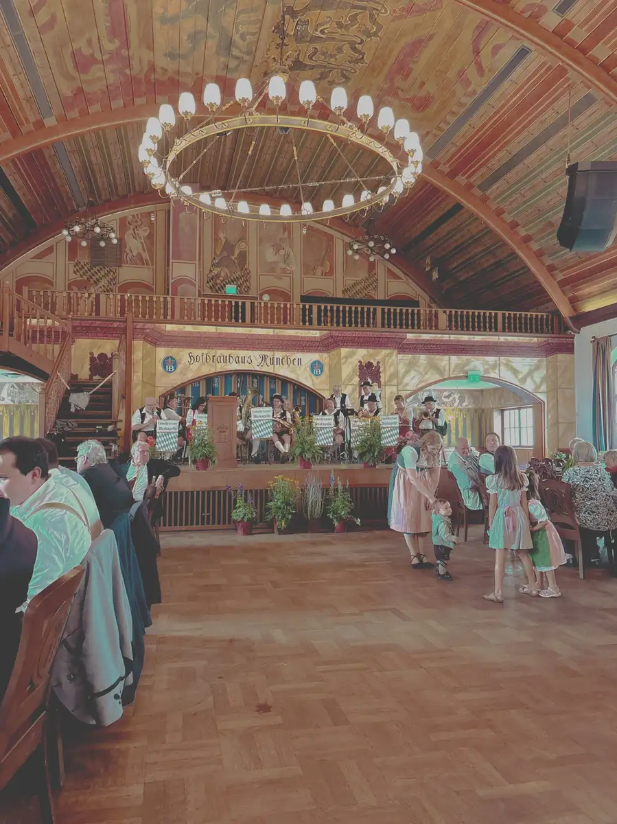 Menschen in traditioneller Kleidung genießen Musik und Essen in einem großen, verzierten Saal mit Holzdecken und einem großen Kronleuchter.